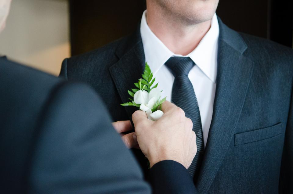 A buttonhole being pinned to a groom's dark wedding suit